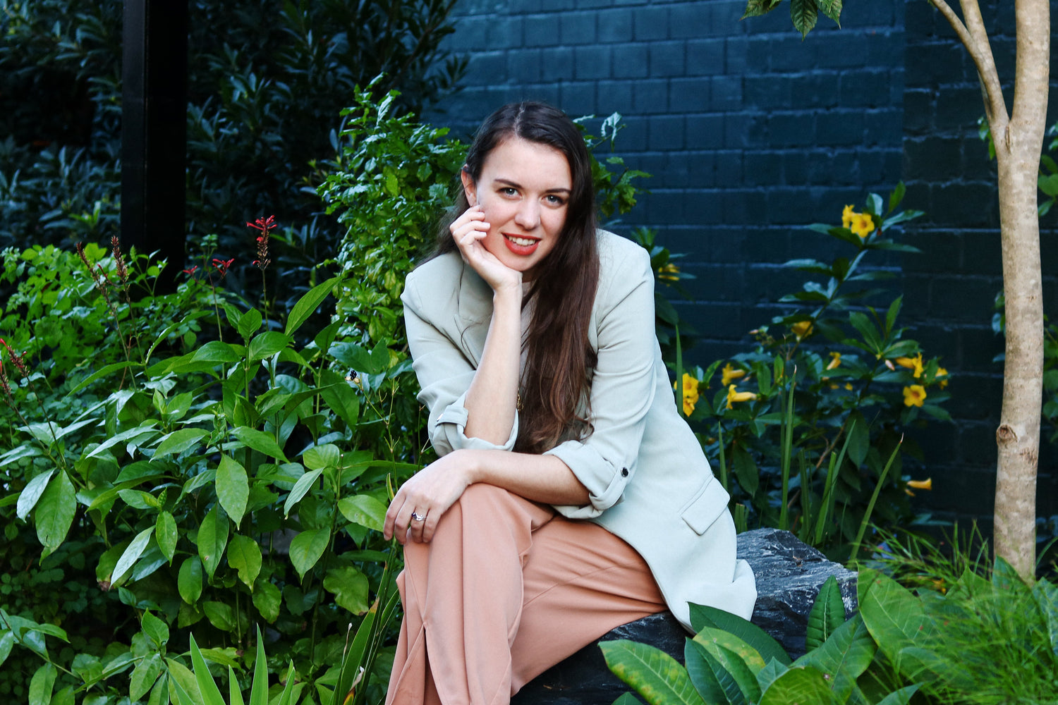 Woman sitting in a garden with greenery and a dark wall in the background